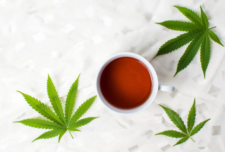 Cannabis leaves surrounding a cup of tea.